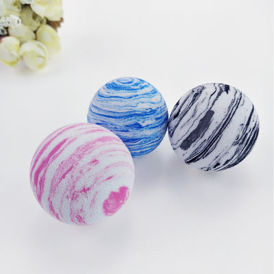 Black and white marbled EVA foam ball, a pet toy, on a white background with blurred flowers.