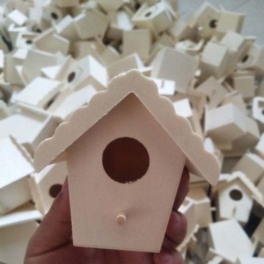 Unfinished wooden birdhouse with a circular entrance hole and a small perch, held by a hand.