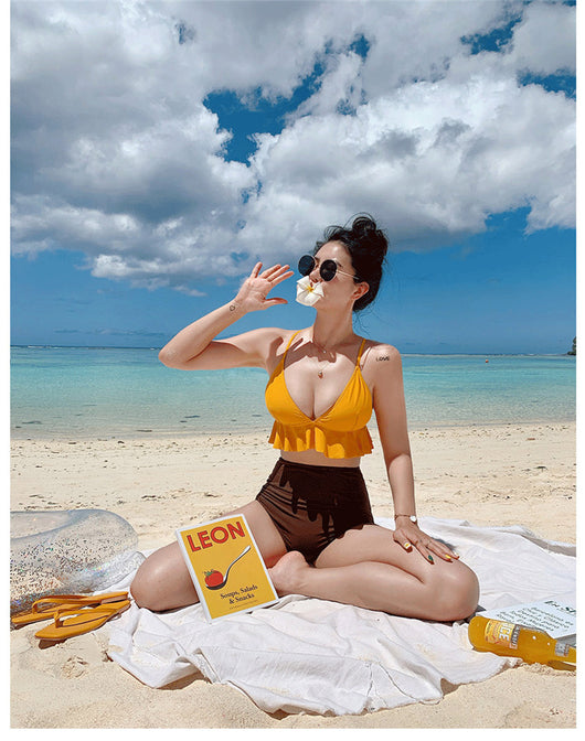 Woman in a yellow ruffled bikini top and dark brown high-waisted bottoms sitting on a beach. - Image 11