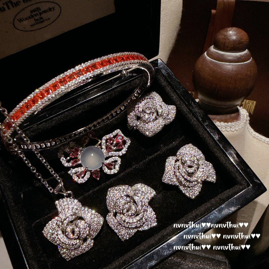 Pair of sparkling rose-shaped stud earrings, encrusted with clear gemstones, displayed in a brown jewelry box. - Image 7