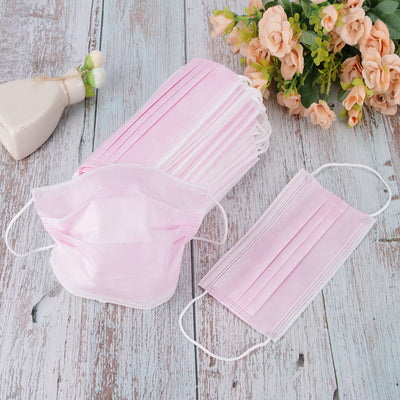 Stack of pink disposable non-woven face masks, with one unfolded and one folded, on a light wood surface. - Image 4