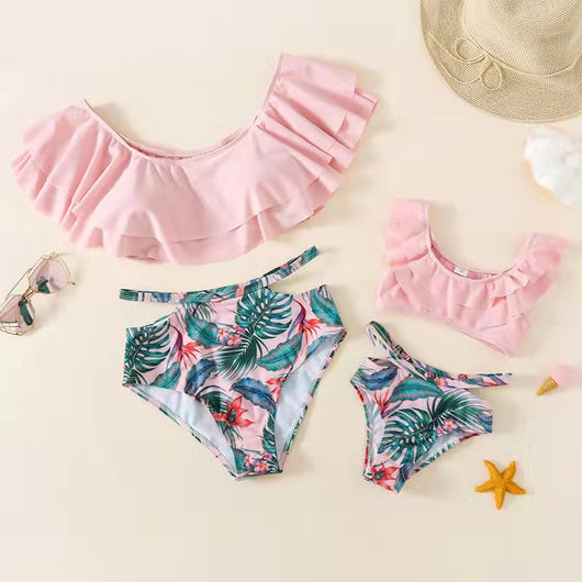 Family matching swimsuits with pink tropical floral and leaf print. Includes women's ruffled bikini, girl's one-piece, and men's/boy's swim shorts. - Image 2