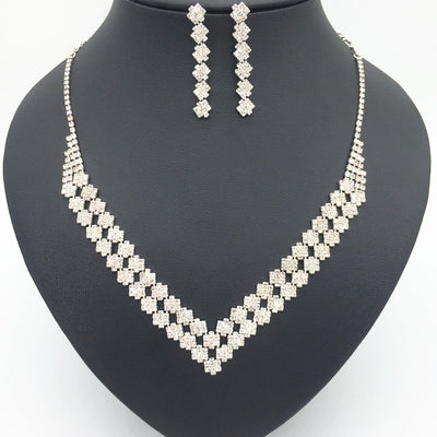 Sparkling silver-tone rhinestone necklace and matching dangle earrings set, featuring a V-shaped design on a black bust.