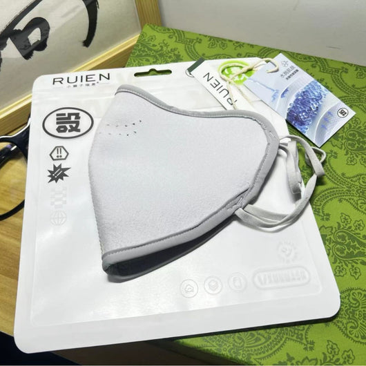 Dark gray cotton head-mounted mask with adjustable ear loops, shown in packaging on a patterned green surface. - Image 3