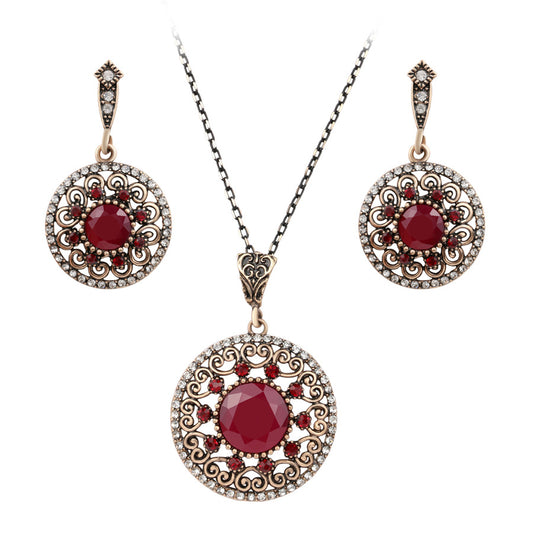 Vintage-style jewelry set with a necklace and matching drop earrings. Features red and clear gemstones in an antique gold-tone filigree design.