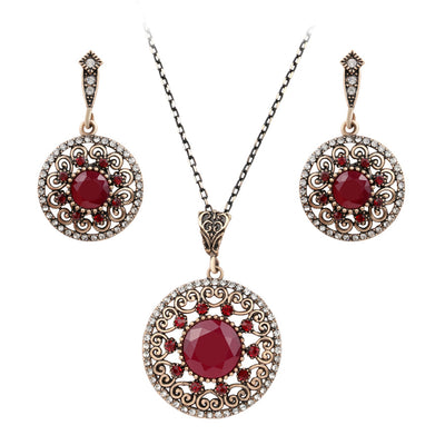 Vintage-style jewelry set with a necklace and matching drop earrings. Features red and clear gemstones in an antique gold-tone filigree design.