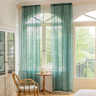 Close-up of a dark green lace curtain with an intricate floral and scrollwork pattern on sheer polyester fabric.