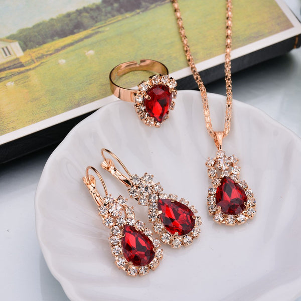 Rose gold-toned necklace, earrings, and ring set with large oval clear gemstones surrounded by smaller stones.