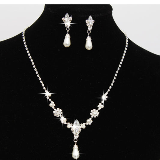 Purple rhinestone and faux pearl necklace and drop earrings set on a black display. Features silver-tone settings.