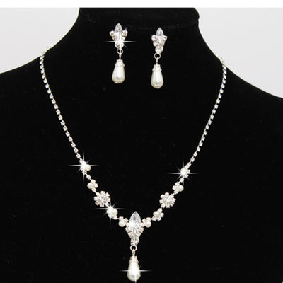 Purple rhinestone and faux pearl necklace and drop earrings set on a black display. Features silver-tone settings.