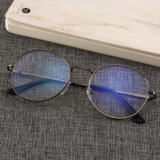 Gold round-frame anti-blue light glasses with clear resin lenses on a gray textured surface next to a notebook. - Image 3