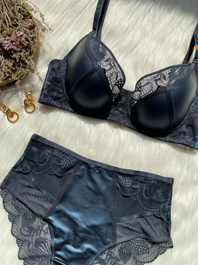 Black lace and smooth fabric bra and matching panties set, featuring a decorative ring, on a white faux fur surface. - Image 7