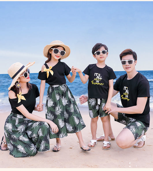 Family of four in matching black and green tropical print outfits on a beach, featuring t-shirts, shorts, skirt, and wide-leg pants. - Image 6