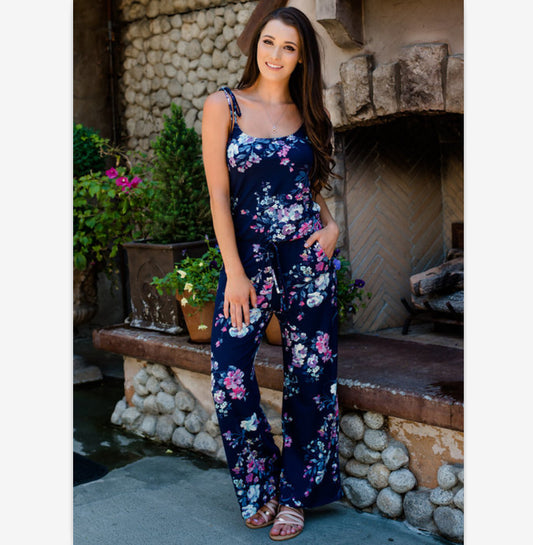 Woman wearing a navy blue floral wide-leg jumpsuit with pink and white flowers, tie-shoulder straps, and a drawstring waist. - Image 2