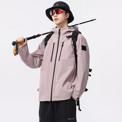 Man wearing a black windproof and waterproof outdoor jacket with a hood, sports sunglasses, and a bucket hat, holding a trekking pole.