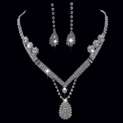 Sparkling silver-toned bridal necklace and matching drop earrings set with clear rhinestones. The necklace features a V-shape and a teardrop pendant, while the