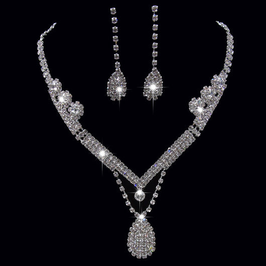 Sparkling silver-toned bridal necklace and matching drop earrings set with clear rhinestones. The necklace features a V-shape and a teardrop pendant, while the