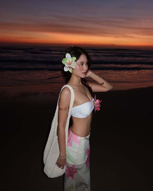 Woman in a white tube top with pink flower and a sheer floral maxi skirt, posing on a beach at sunset. - Image 9