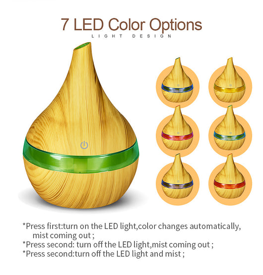 Dark wood grain LED essential oil diffuser with a blue light band and touch switch, shown with a hand operating it. Includes a bundle of 10 white filter sticks. - Image 3