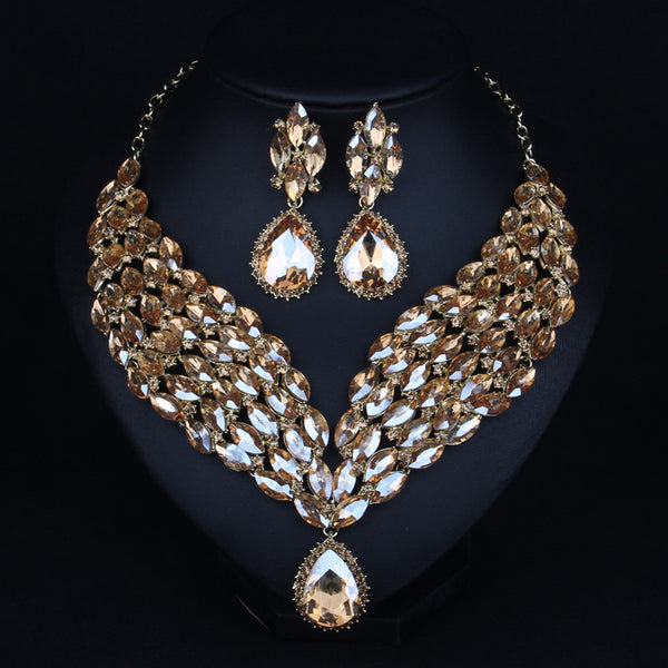 Green and teal rhinestone necklace and matching dangle earrings set on a black jewelry stand.
