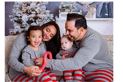 Family of four in matching grey long-sleeve tops and red striped pants, posing in a festive holiday setting.