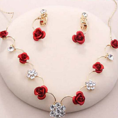 Red rose and clear crystal necklace and matching earrings set on a white jewelry bust, with a pink background.