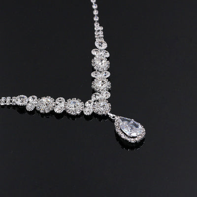 Sparkling silver-toned necklace and matching teardrop earrings set with clear stones, displayed on a black stand. - Image 5