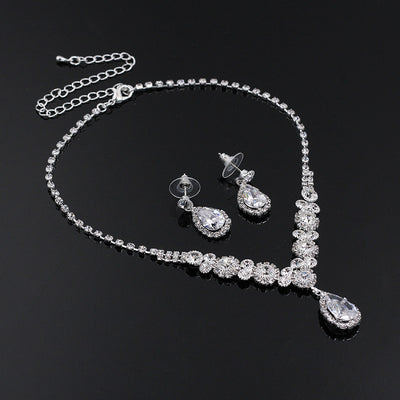 Sparkling silver-toned necklace and matching teardrop earrings set with clear stones, displayed on a black stand. - Image 4