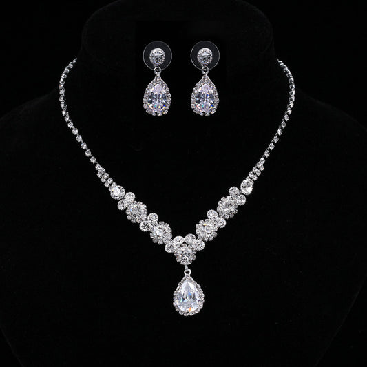 Sparkling silver-toned necklace and matching teardrop earrings set with clear stones, displayed on a black stand.