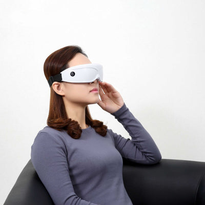 White and black eye massager with a goggle-like design, featuring a white frame and dark lenses, on a wooden surface. - Image 8