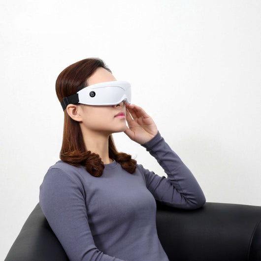 White and black eye massager with a goggle-like design, featuring a white frame and dark lenses, on a wooden surface. - Image 8
