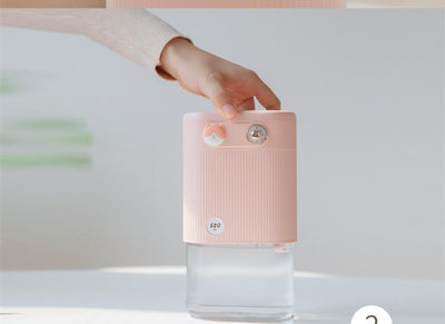 White cylindrical humidifier with ribbed texture, clear base, brown bear button, and silver dial, emitting mist on a white table. - Image 4