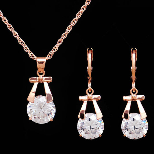 Rose gold-toned jewelry set with a necklace and matching dangle earrings, each featuring a round clear crystal.