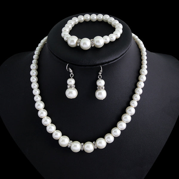 Three-piece white faux pearl jewelry set with rhinestone accents, including a necklace, drop earrings, and a bracelet.