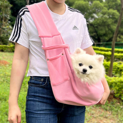 Person in white hoodie carrying a happy white dog in a navy blue pet sling bag outdoors. - Image 34