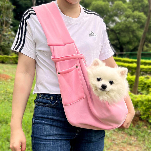 Person in white hoodie carrying a happy white dog in a navy blue pet sling bag outdoors. - Image 34