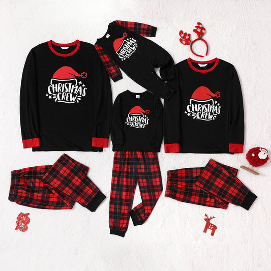 Family of four wearing matching red and black plaid Christmas pajamas with "Christmas CREW" graphic, children in Santa hats.