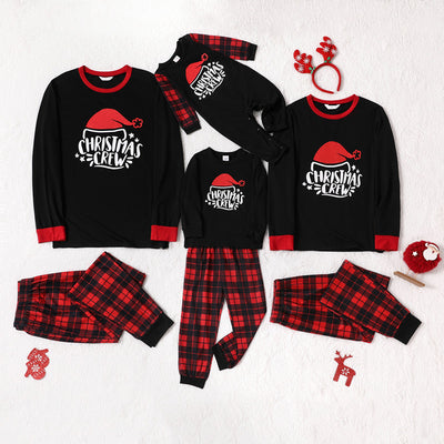 Family of four wearing matching red and black plaid Christmas pajamas with "Christmas CREW" graphic, children in Santa hats.