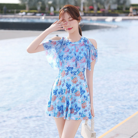 Pink dress-style swimsuit with cold-shoulder ruffles and a vibrant coral and seashell print, modeled by a woman. - Image 4