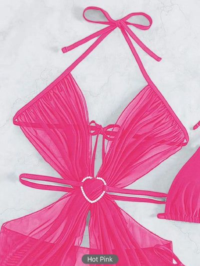 White three-piece halter neck bikini and sheer cover-up set with a heart-shaped embellishment, laid flat on wood. - Image 10