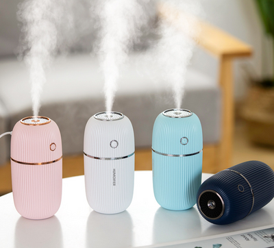 Pink mini ultrasonic air humidifier with ribbed texture and rose gold accents, emitting a fine mist on a white shelf. - Image 2