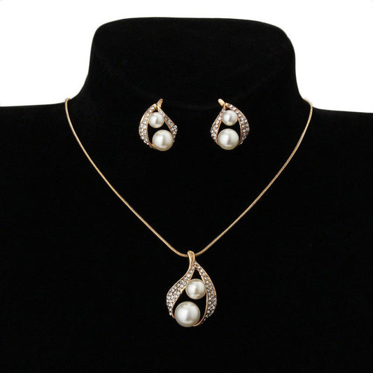 Gold-tone teardrop necklace and matching stud earrings set with white pearls and clear rhinestones, displayed on black.