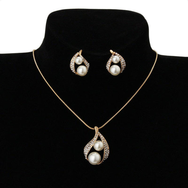 Gold-tone teardrop necklace and matching stud earrings set with white pearls and clear rhinestones, displayed on black.
