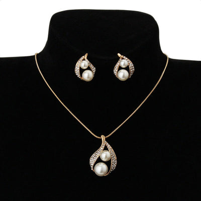 Gold-tone teardrop necklace and matching stud earrings set with white pearls and clear rhinestones, displayed on black.