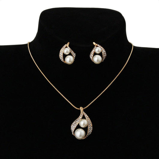 Gold-tone teardrop necklace and matching stud earrings set with white pearls and clear rhinestones, displayed on black.