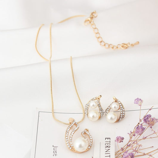 Gold-tone teardrop necklace and matching stud earrings set with white pearls and clear rhinestones, displayed on black. - Image 2