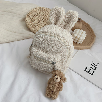 Pink fuzzy mini backpack with bear ears and a small white teddy bear keychain on a white bed. - Image 9