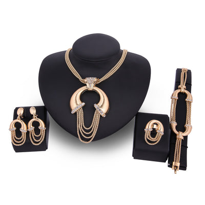 Four-piece gold-tone bridal jewelry set with crystal accents, including a statement necklace, dangling earrings, bracelet, and ring.