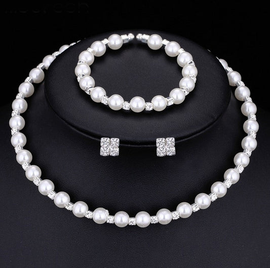 Bridal three-piece jewelry set with white pearls and clear rhinestones, including a necklace, bracelet, and square stud earrings.