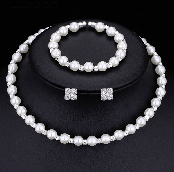 Bridal three-piece jewelry set with white pearls and clear rhinestones, including a necklace, bracelet, and square stud earrings.